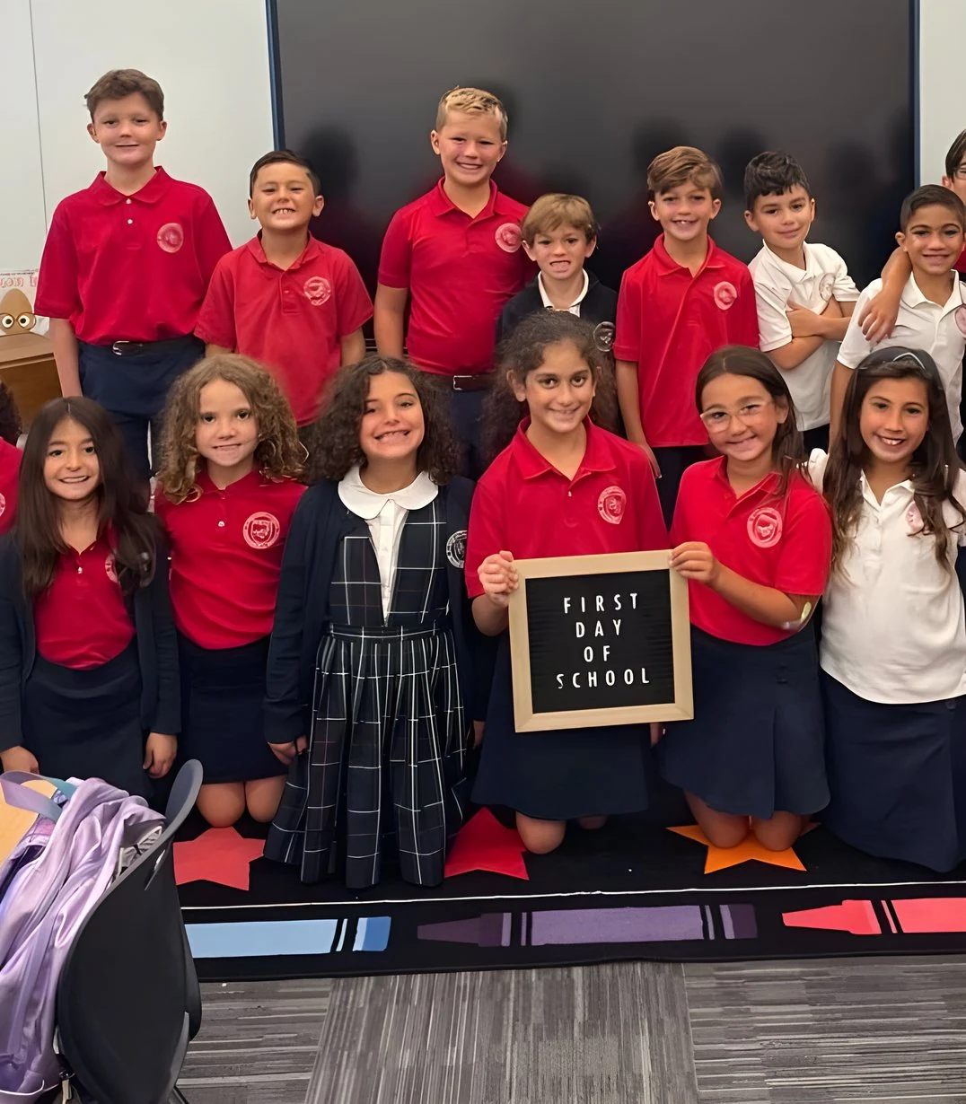 Students holding a "First Day of School" sign in their classroom