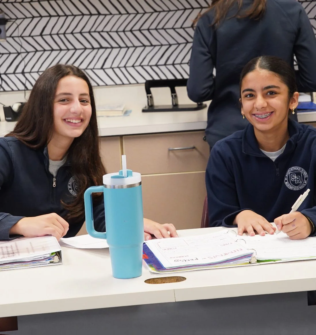 Two academy students smiling while working at a desk