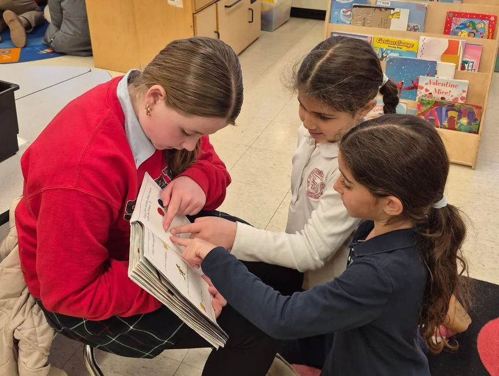 Older and younger students reading a book together