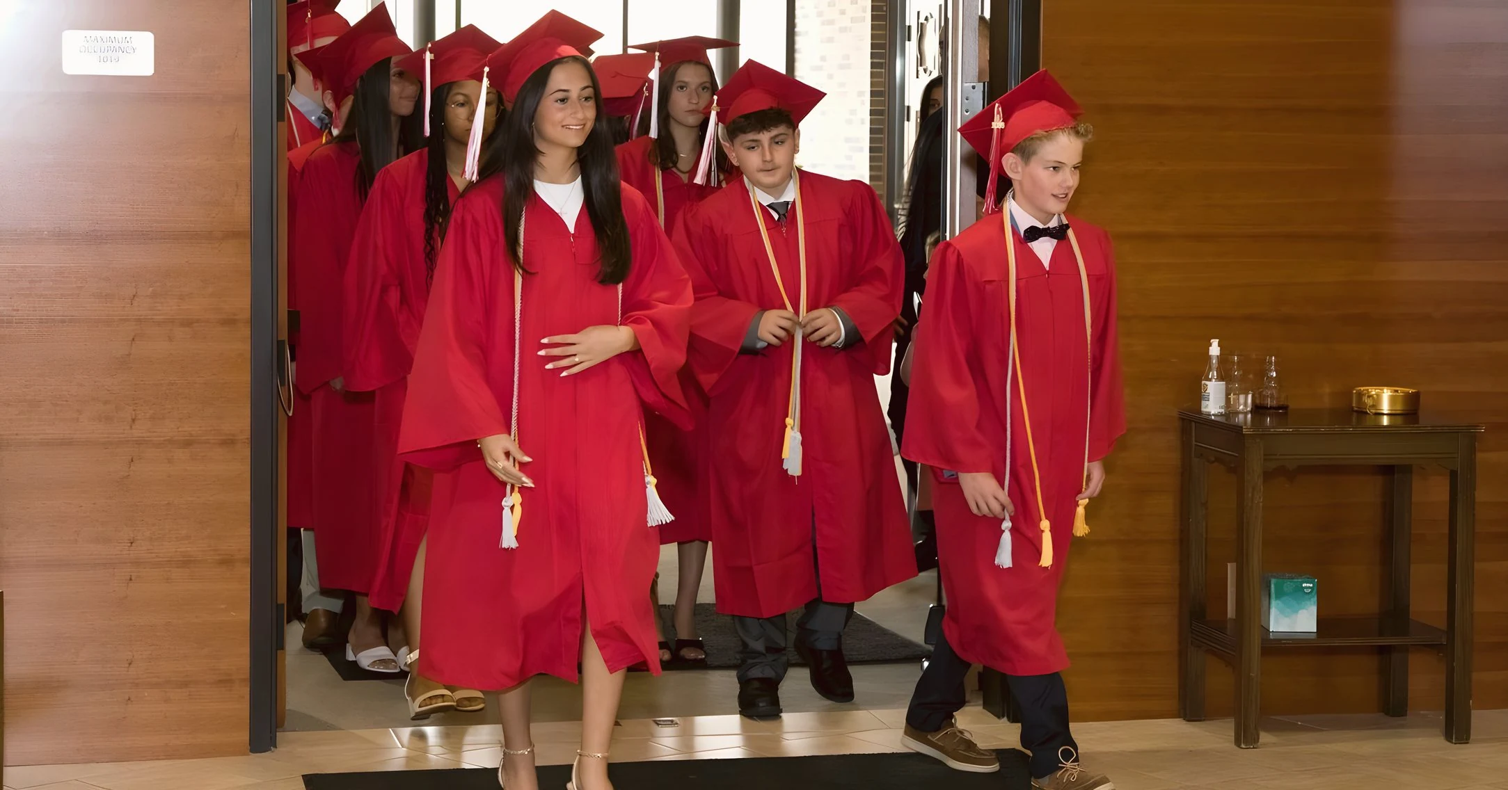 8th grade graduates in red caps and gowns processing into church